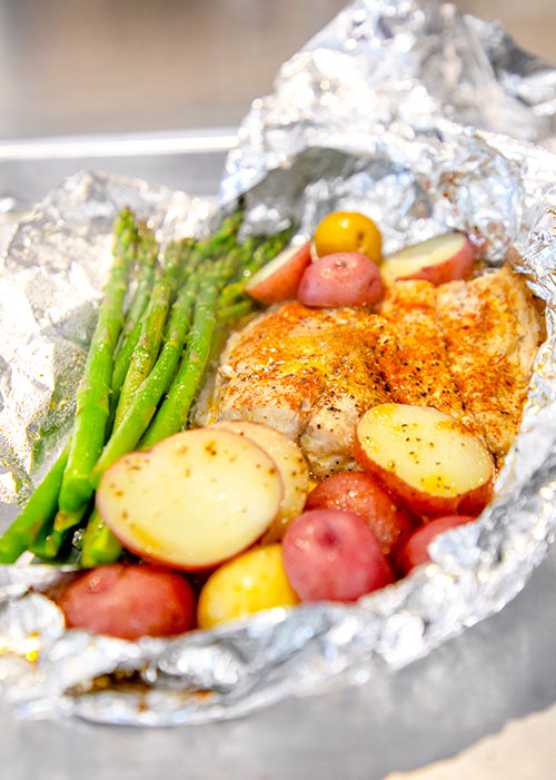 Photo of foil packet open with cooked bluefish, potatoes and asparagus.
